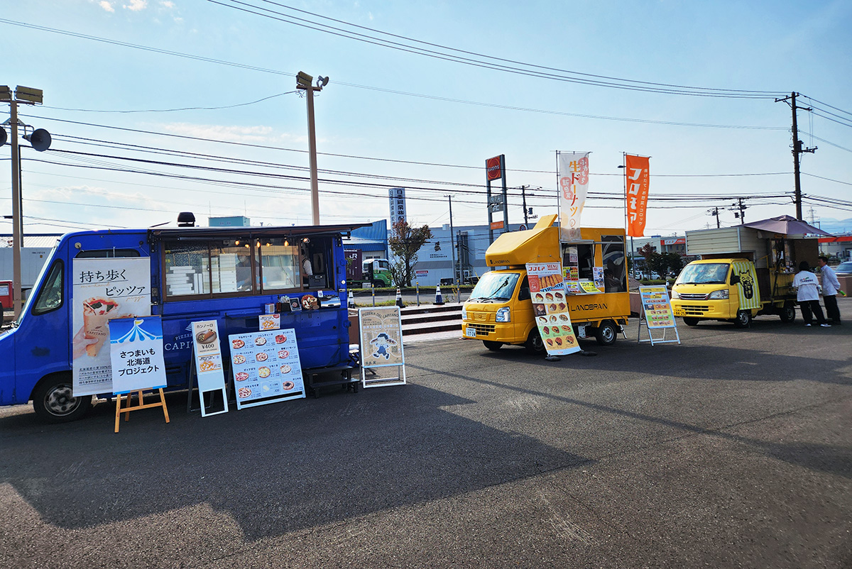 快晴の空の下、キッチンカーが3台並んでいる。左からPIZZERIA DEL CAPITANO(ピッツェリア デル カピターノ)、コロモア、バケネコーヒーのキッチンカーだ。